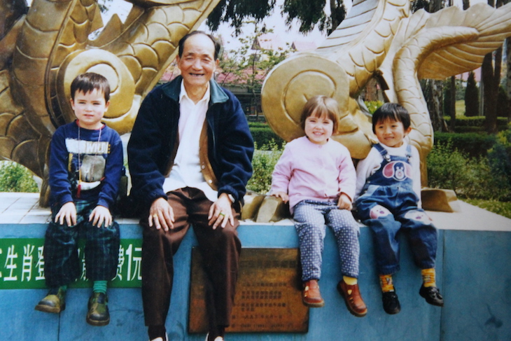 Three children sit with their grandfather in front of a dragon monument in Yunnan, China