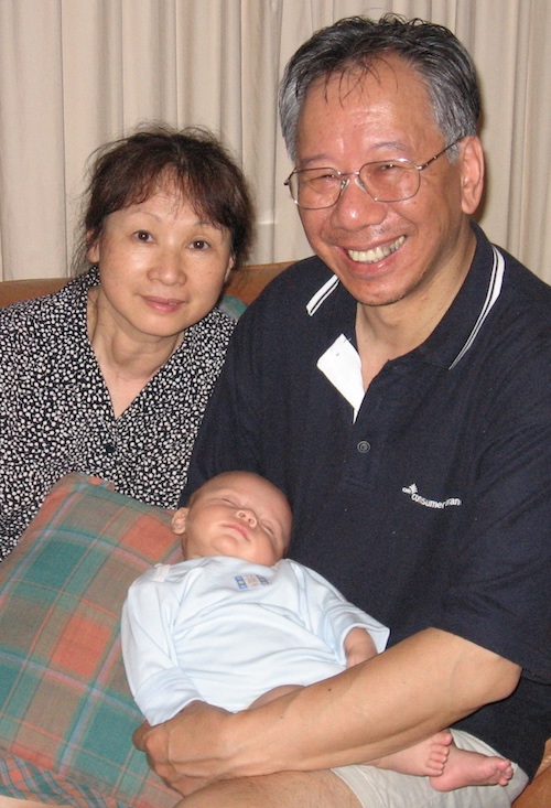 Smiling Chinese grandparents hold their baby grandson