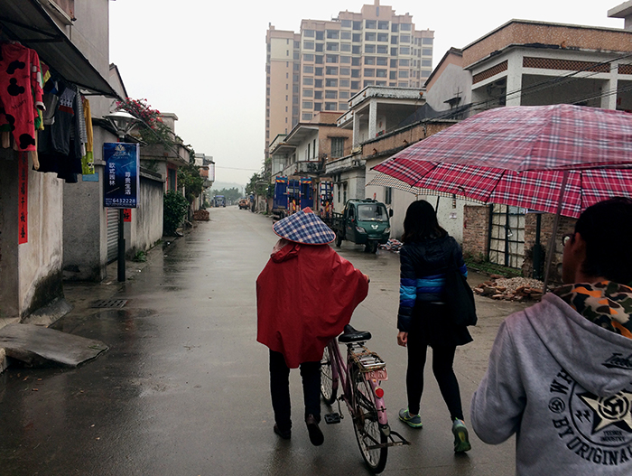 Chinese villager walks with a bicycle down a rainy street