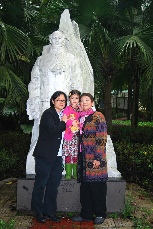 Chinese family smiles in front of a statue of the first Chinese man at the North Pole against a backdrop of palm trees