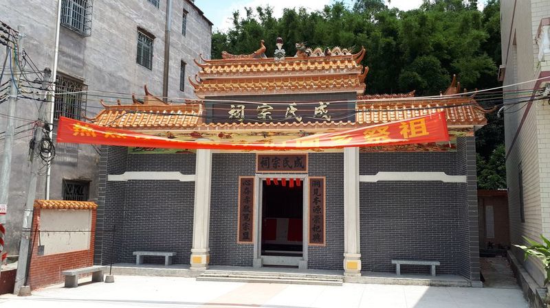 A newly completed 成Chinese ancestral hall with a dark grey brick façade, orange roof tiles, and a red banner. 