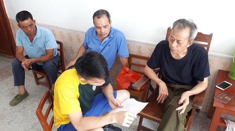 4 men looking at qiaopi 侨批 letters. Three older men are seated against the wall while 1 younger man is seated perpendicular to them, asking about the letters. 